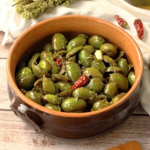 Seasoned cracked green olives in earthenware bowl.
