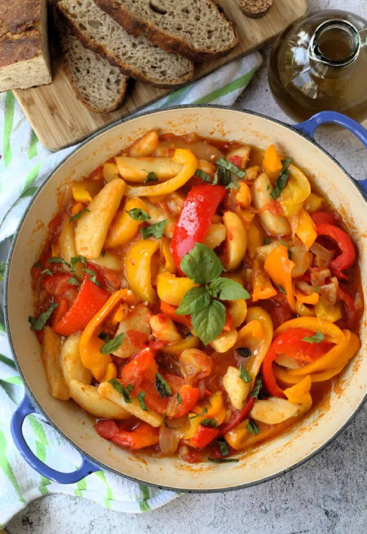 Italian stewed peppers with potatoes in large skillet next to bread slices.