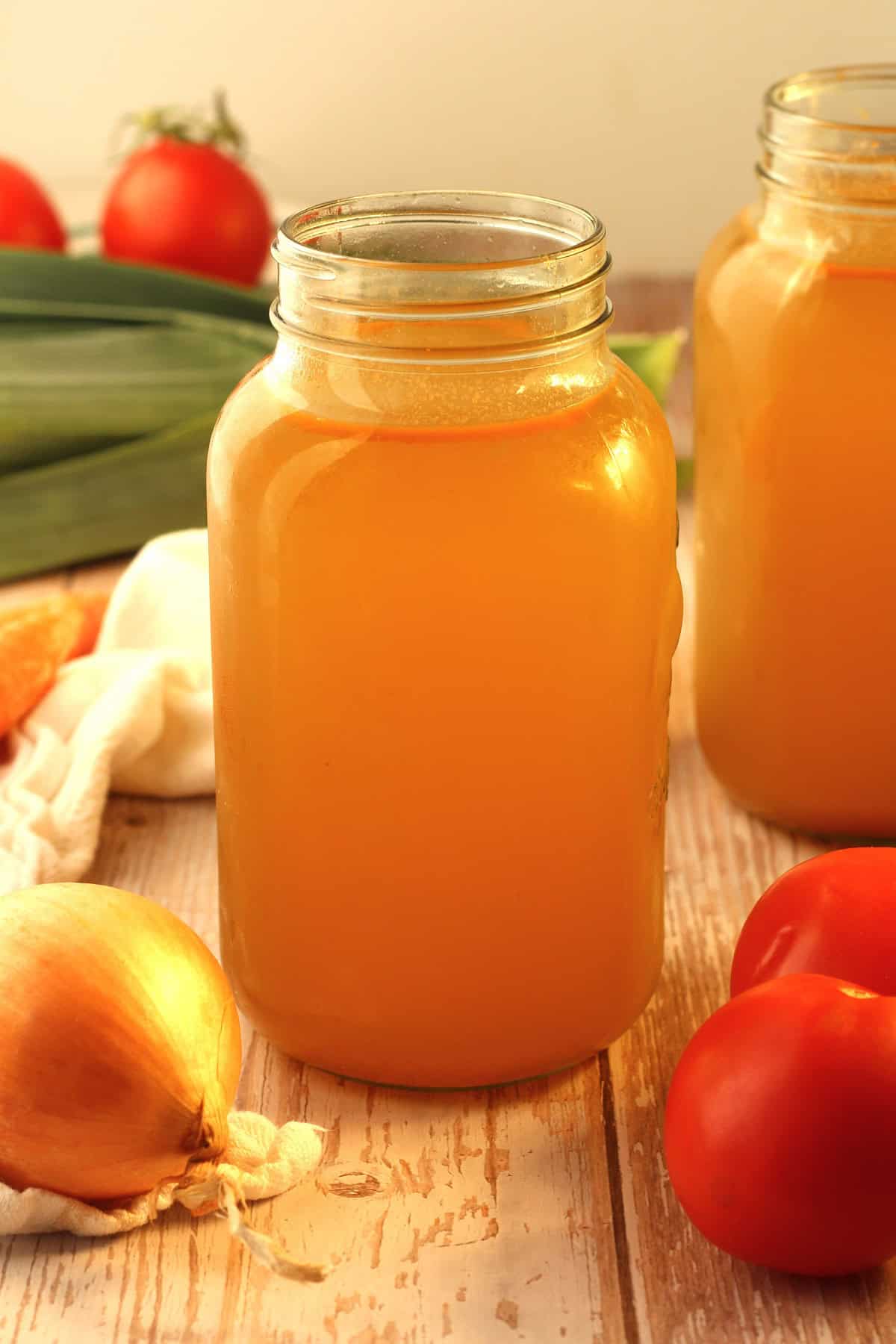 Homemade vegetable broth in mason jar surrounded by vegetables.