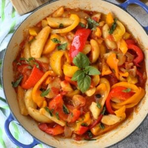 Italian stewed peppers with tomatoes and potatoes topped with basil in blue skillet.