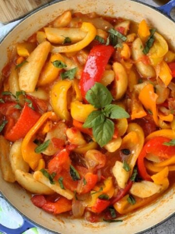 Italian stewed peppers with tomatoes and potatoes topped with basil in blue skillet.