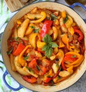 Skillet filled with stewed peppers, potatoes and tomatoes.