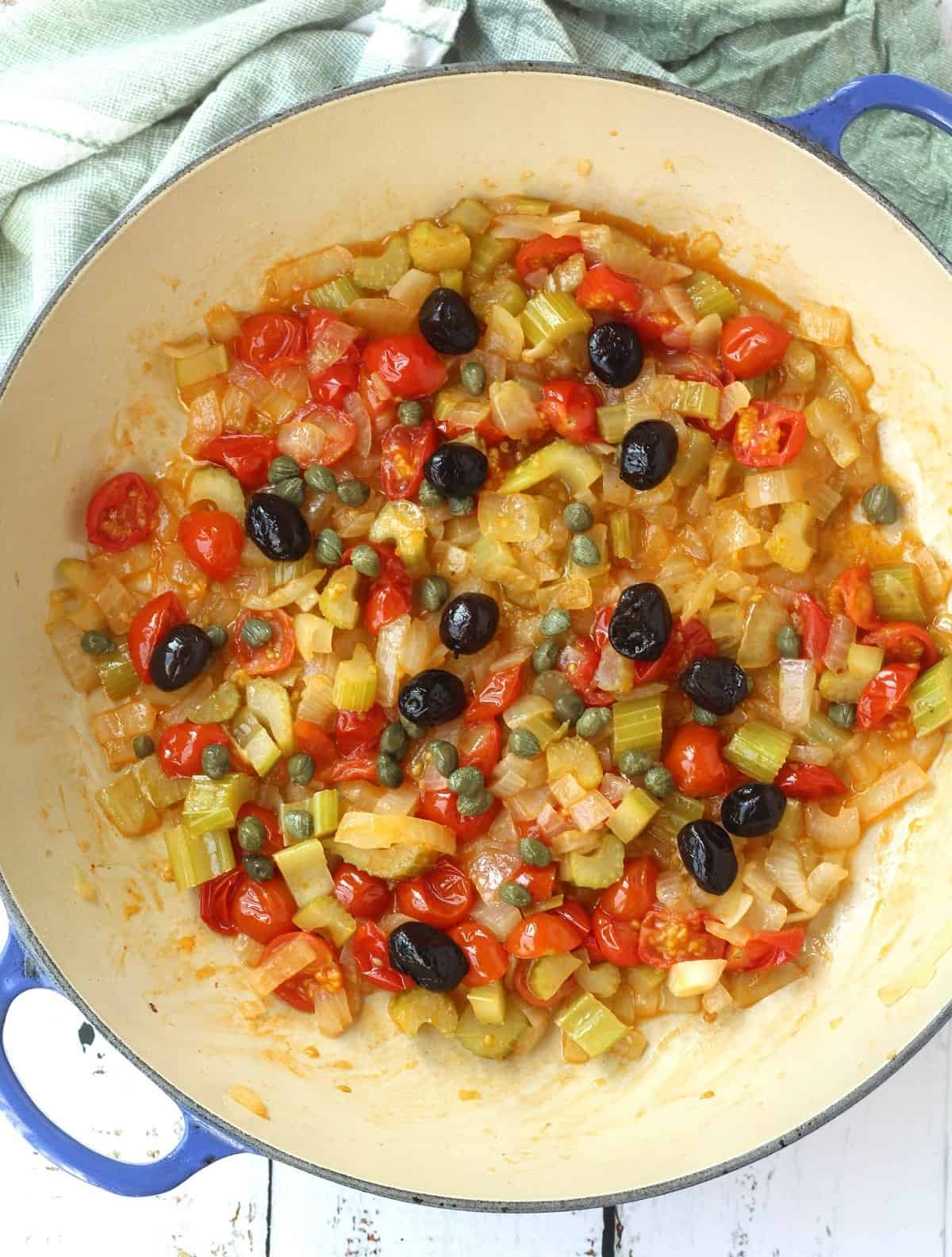 Olives and capers added to skillet for eggplant and swordfish caponata recipe.