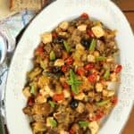 Oval plate filled with eggplant and swordfish caponata with slices of bread on the side.