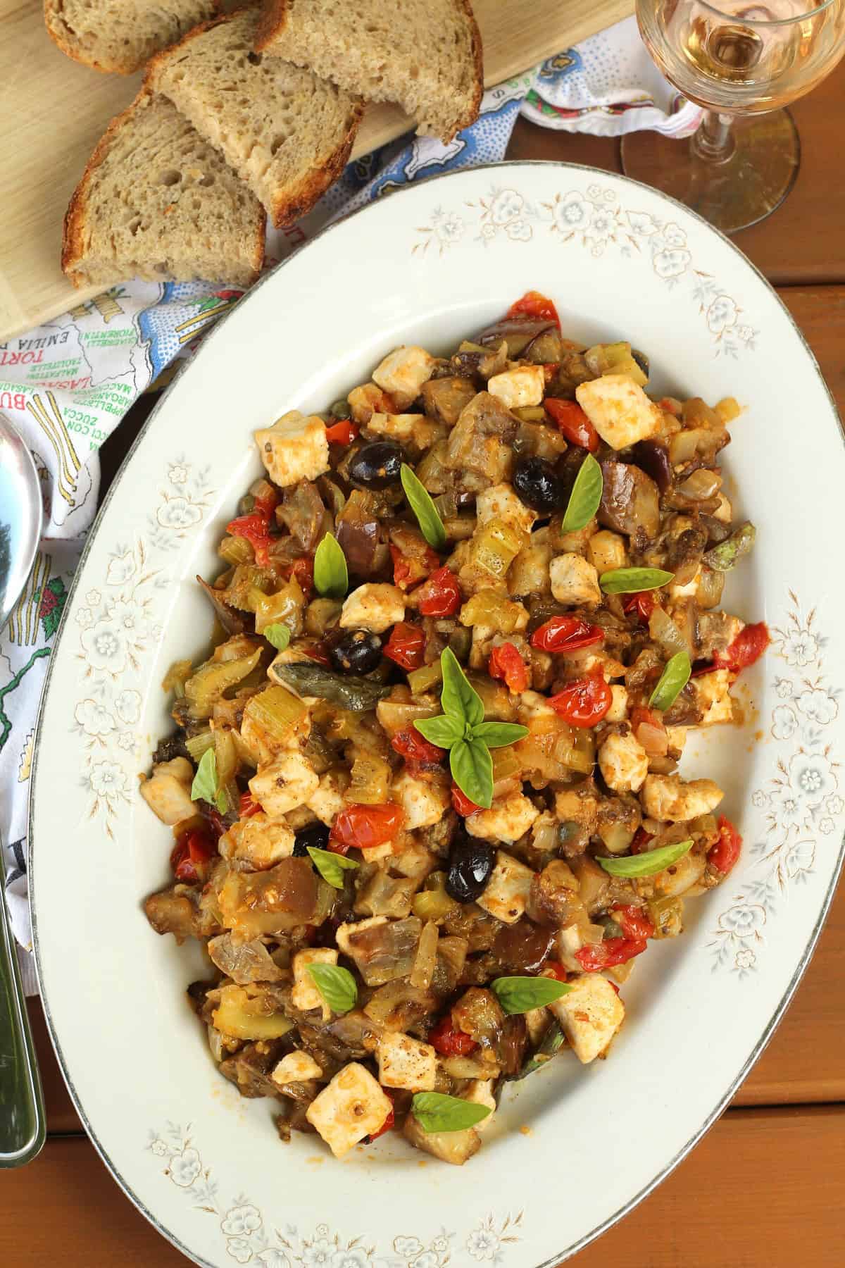 Oval plate filled with eggplant and swordfish caponata with slices of bread on the side.