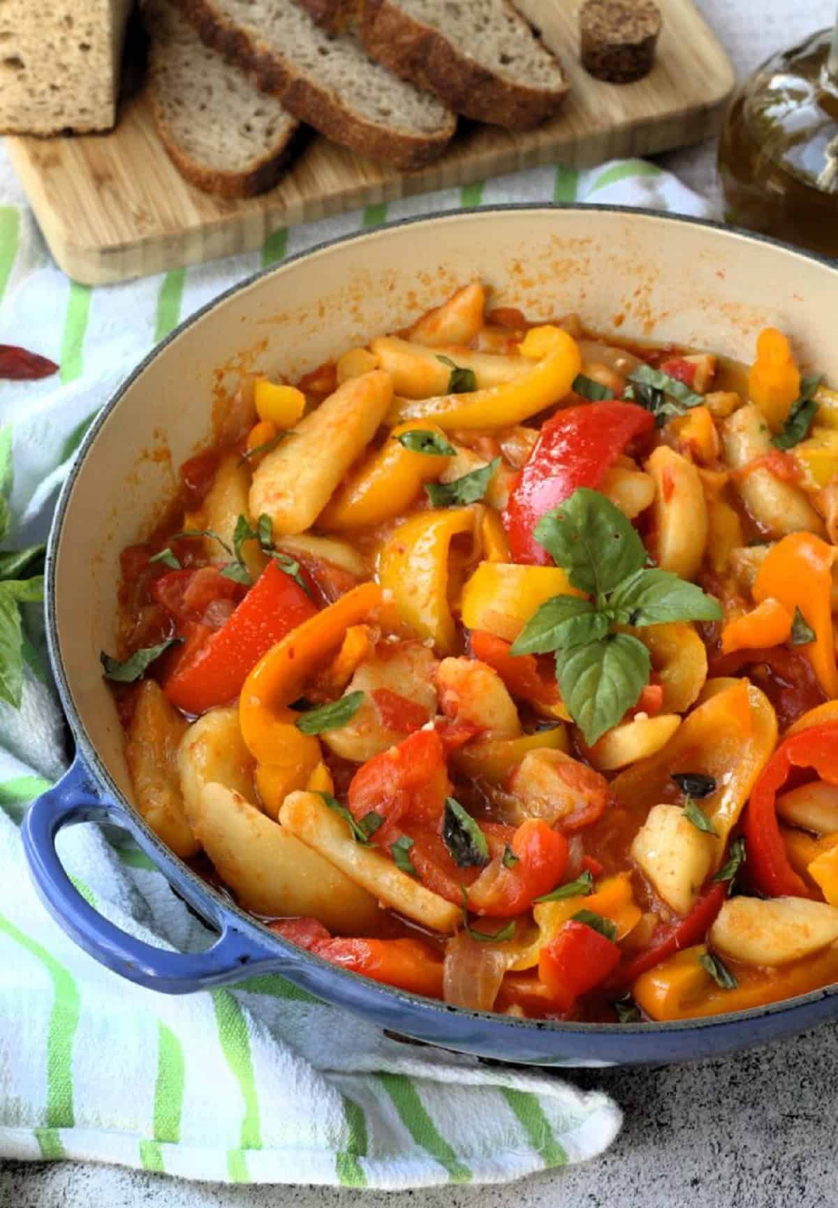 Peperonata recipe with potatoes in large skillet next to slices of bread.