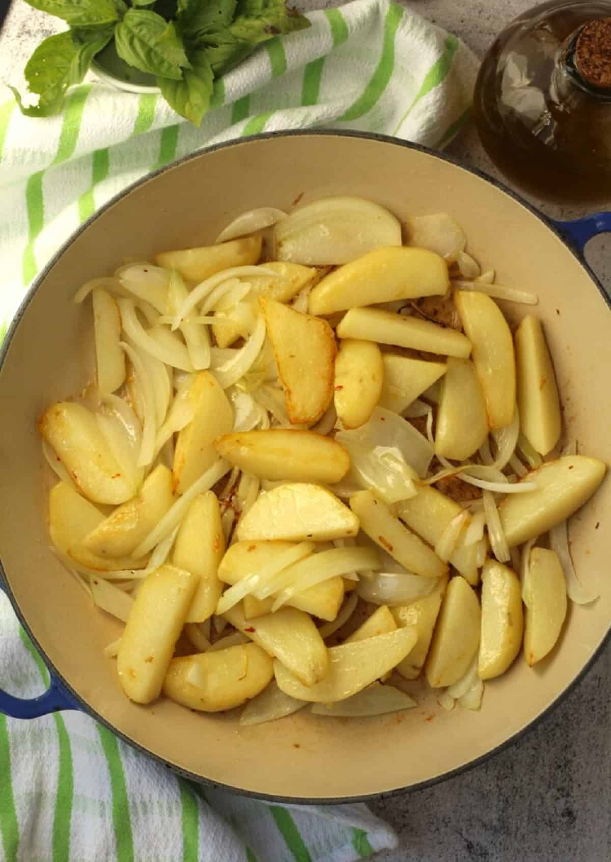 Sautéed potato wedges with sliced onions in skillet for peperonata recipe.