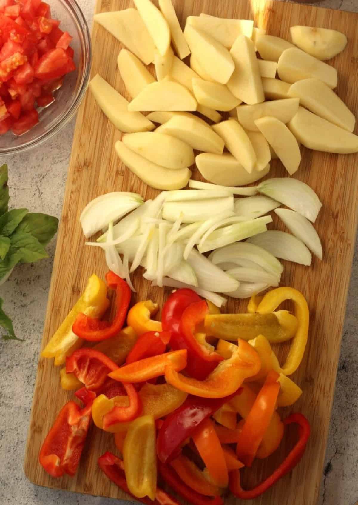 Potatoes cut into wedges, sliced onions and peppers on wood board.