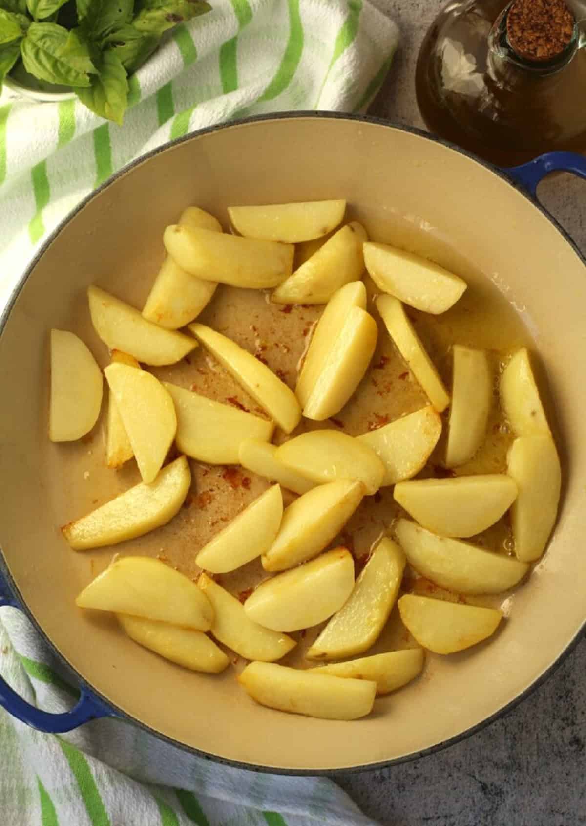 Potato wedges in skillet in olive oil for peperonata recipe.