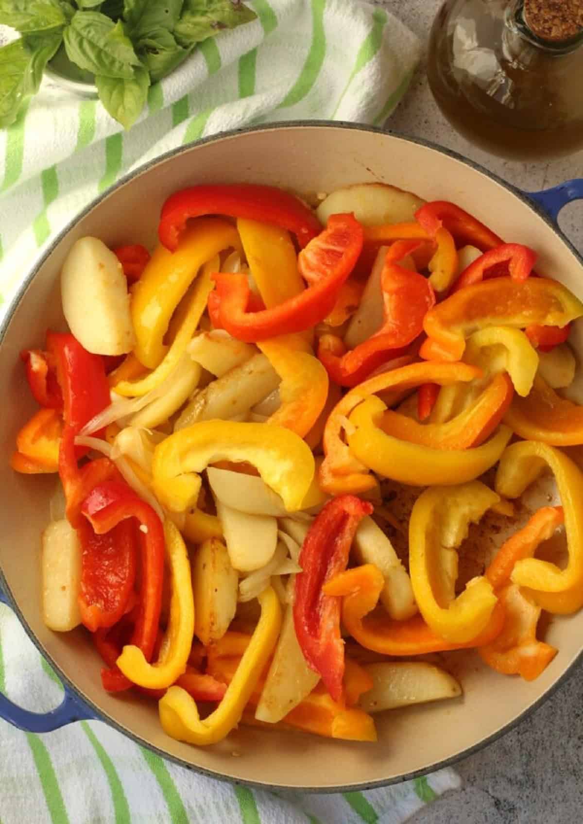 Sliced peppers with onions and potato wedges in skillet for stewed pepper recipe.
