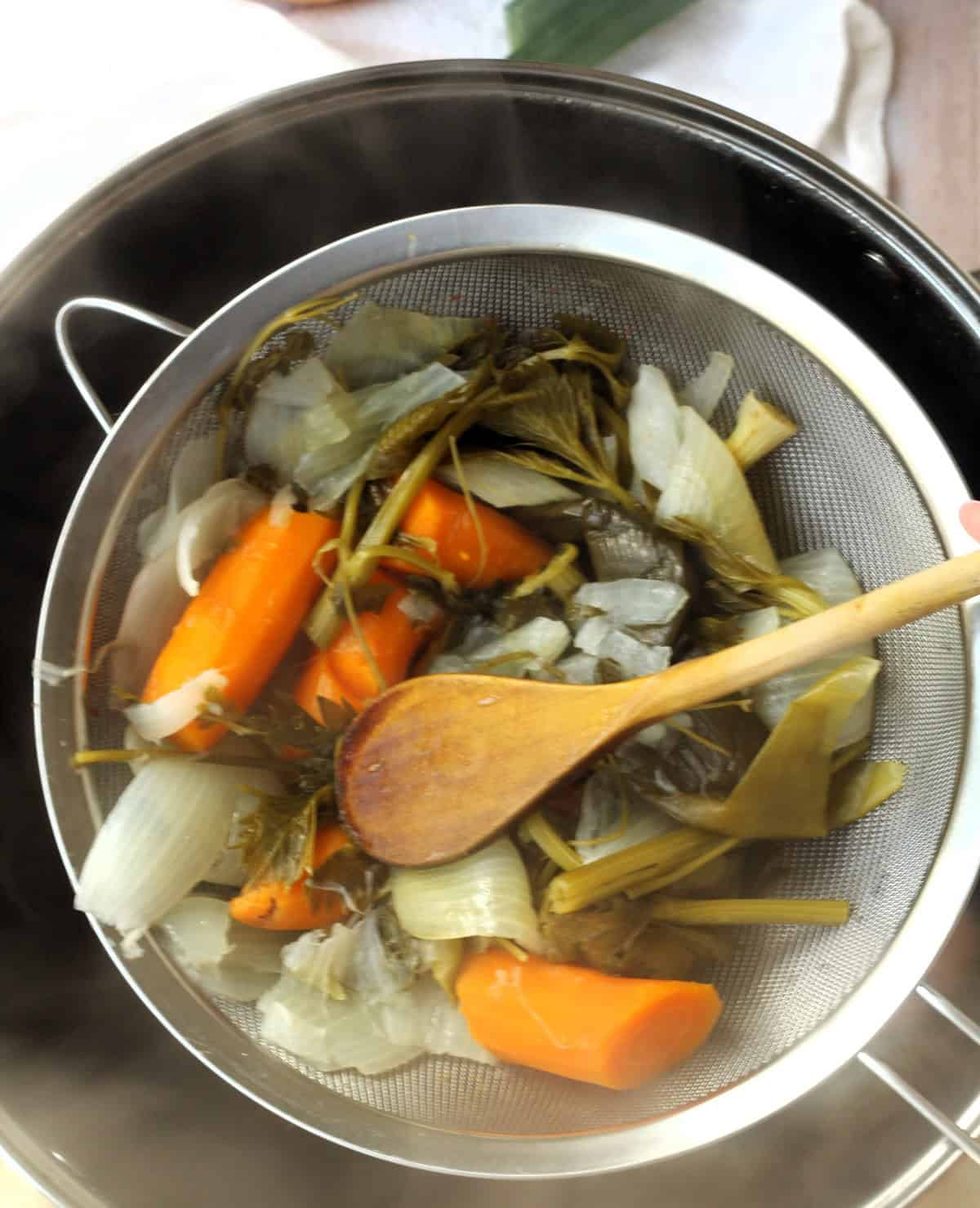 Strained vegetables in sieve over stock pot.