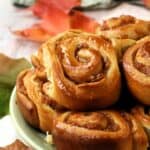 Brioche cinnamon rolls with apples piled on green plate with apples in background.