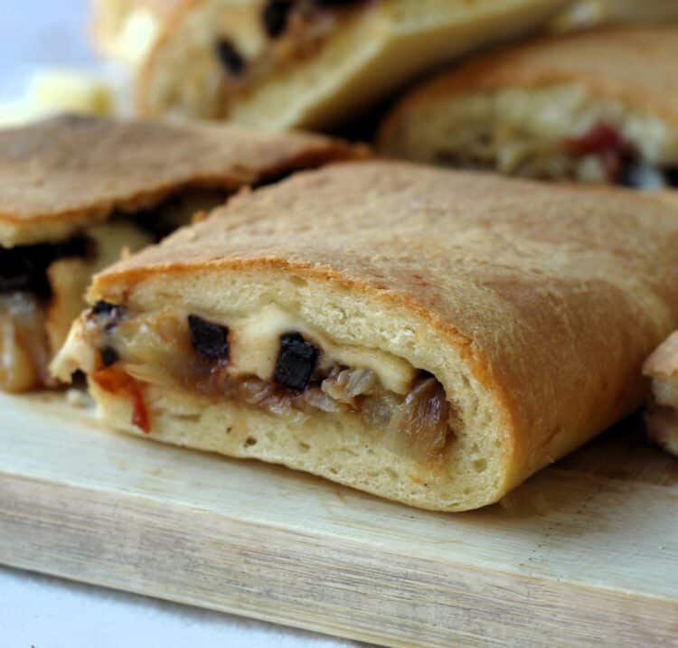 Slice of onion filled cudduruni, Sicilian focaccia, on wood board.