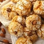 Soft pumpkin almond crinkle cookies piled on white cloth with almonds around them.
