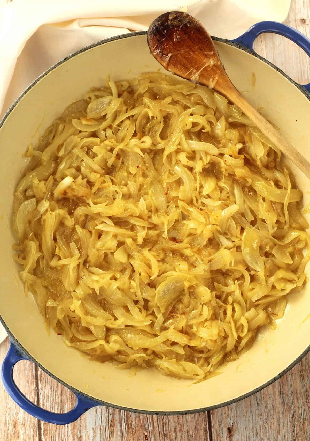 Golden sautéed onions in skillet with wooden spoon for cudduruni filling.