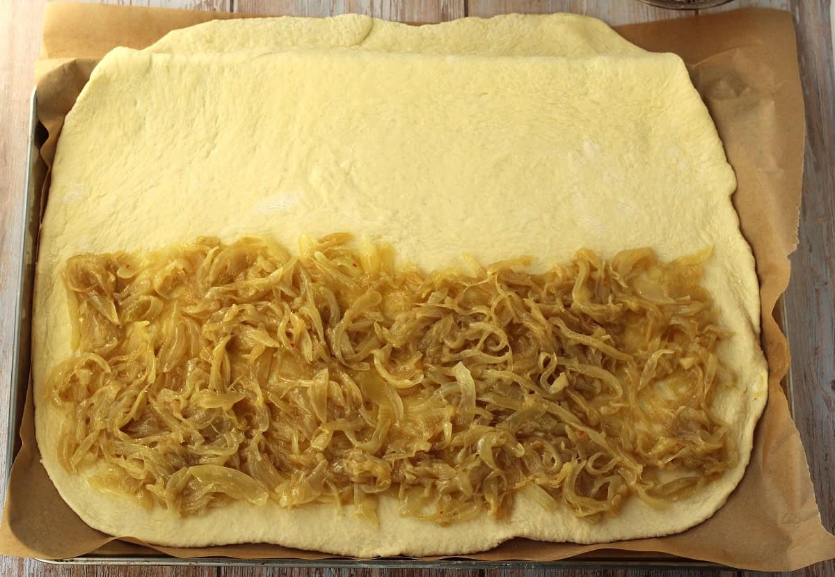 Caramalized onions spread over half of pizza dough.