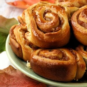 Brioche cinnamon rolls with apples piled on green plate.