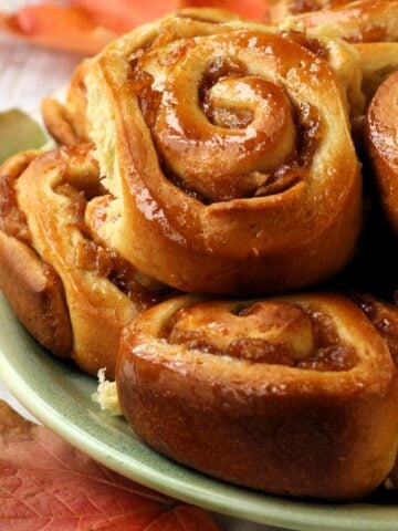 Brioche cinnamon rolls with apples piled on green plate.
