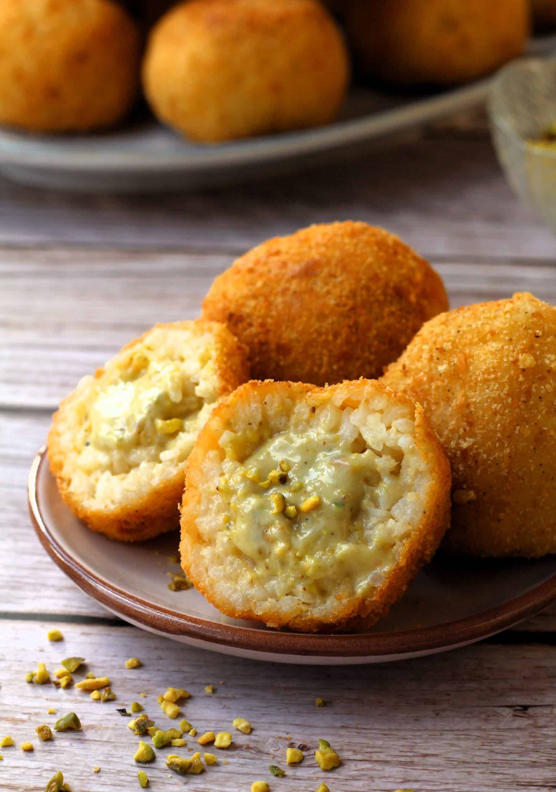 Sicilian pistachio arancini cut in half on plate with whole whole behind it.