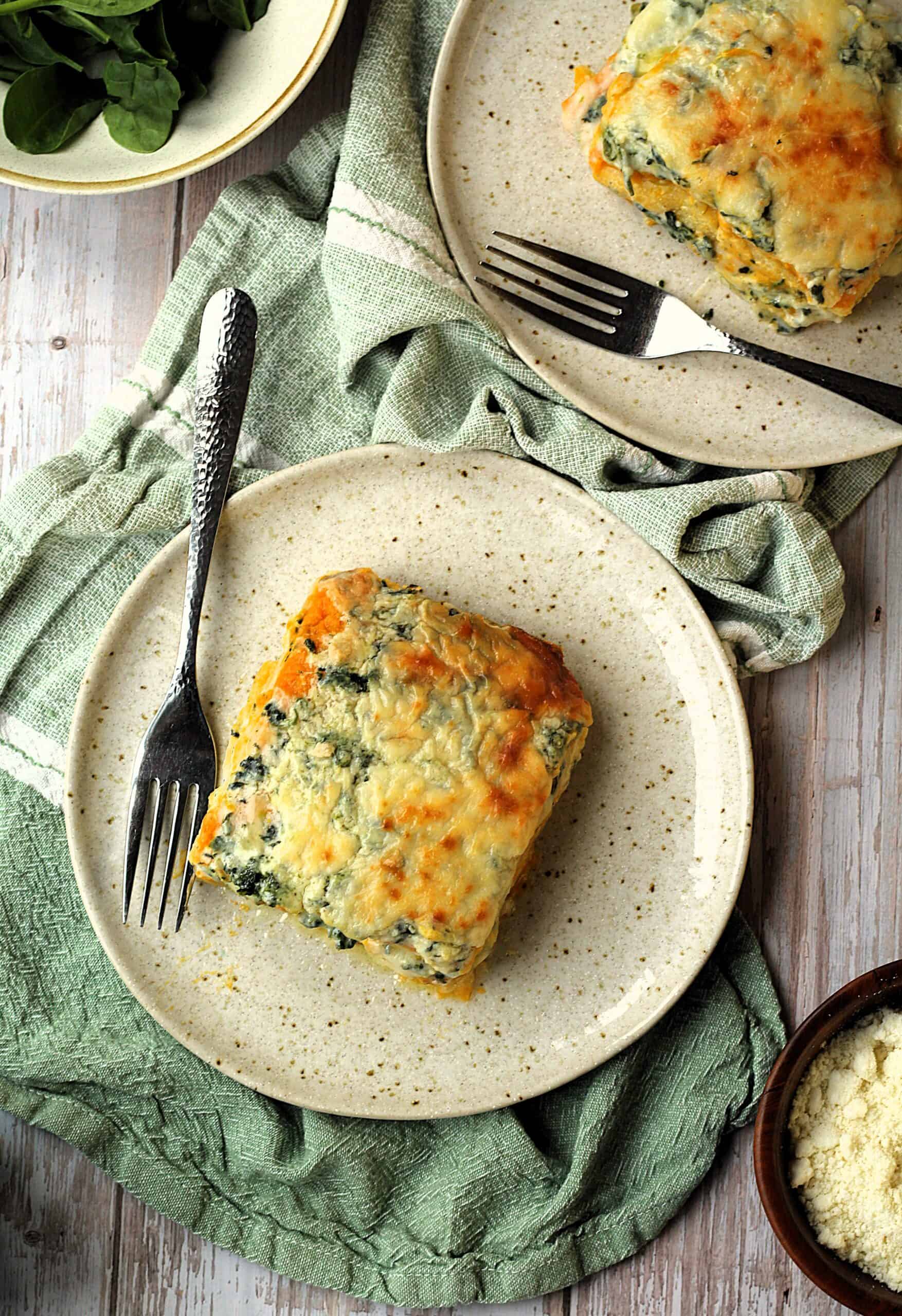 Polenta lasagna with butternut squash and spinach béchamel sauce on round plate with fork surrounded by plates.