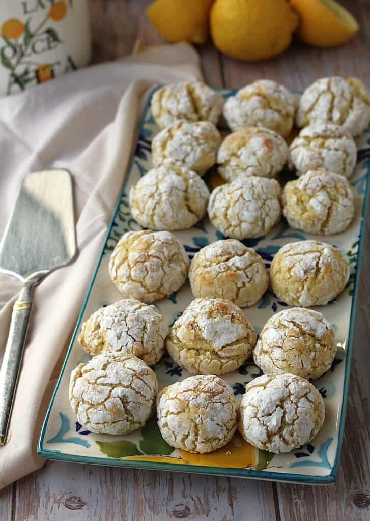 Lemon cookies with almond flour on rectangular plate with lemons behind it.
