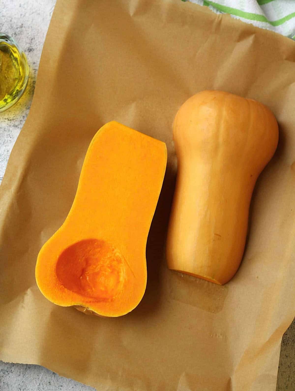 Halved butternut squash without seeds on parchment lined baking sheet.