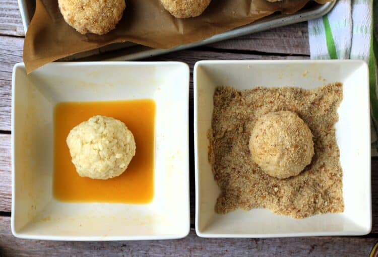 Dredging arancini rice balls in egg wash and bowl of breadcrumbs.
