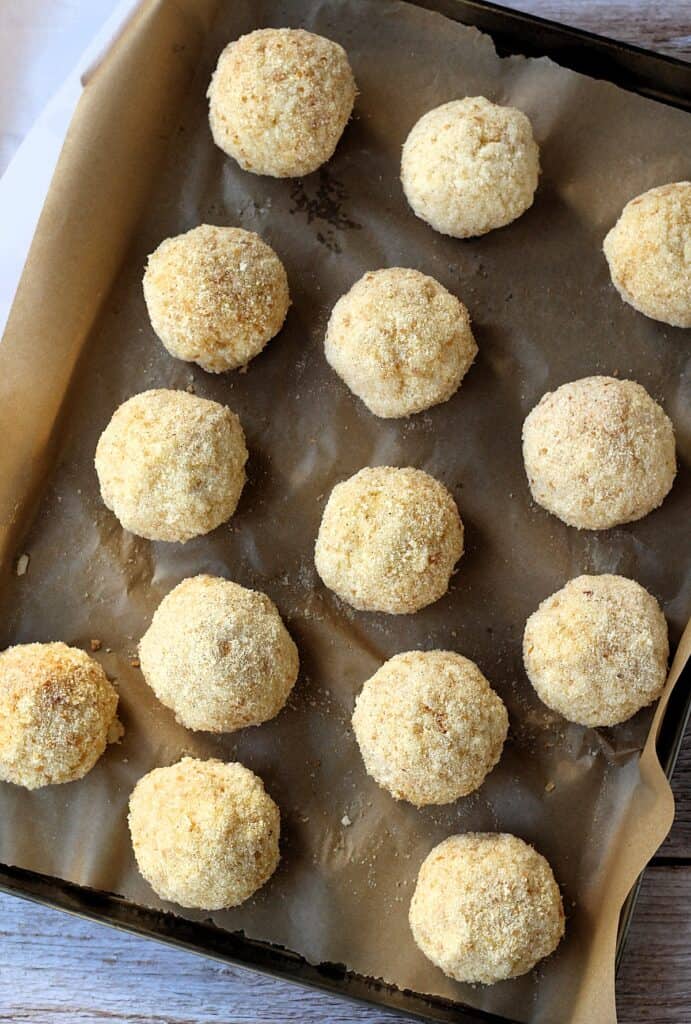 Shaped, breaded arancini balls on baking sheet.