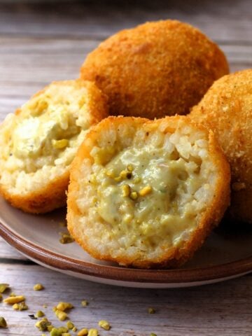 Pistachio arancini cut in half on plate with 2 whole arancini behind it.