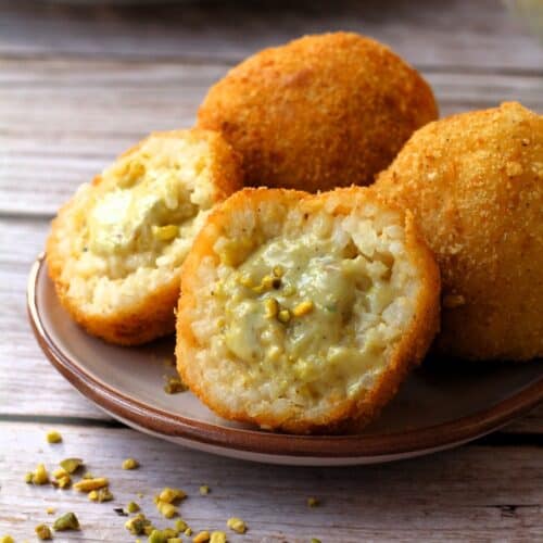 Pistachio arancini cut in half on plate with 2 whole arancini behind it.