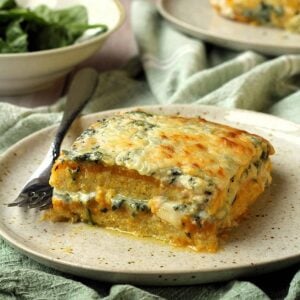 Polenta layered with creamy butternut squash and spinach béchamel sauce on plate with fork.