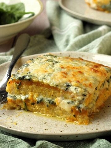 Polenta layered with creamy butternut squash and spinach béchamel sauce on plate with fork.