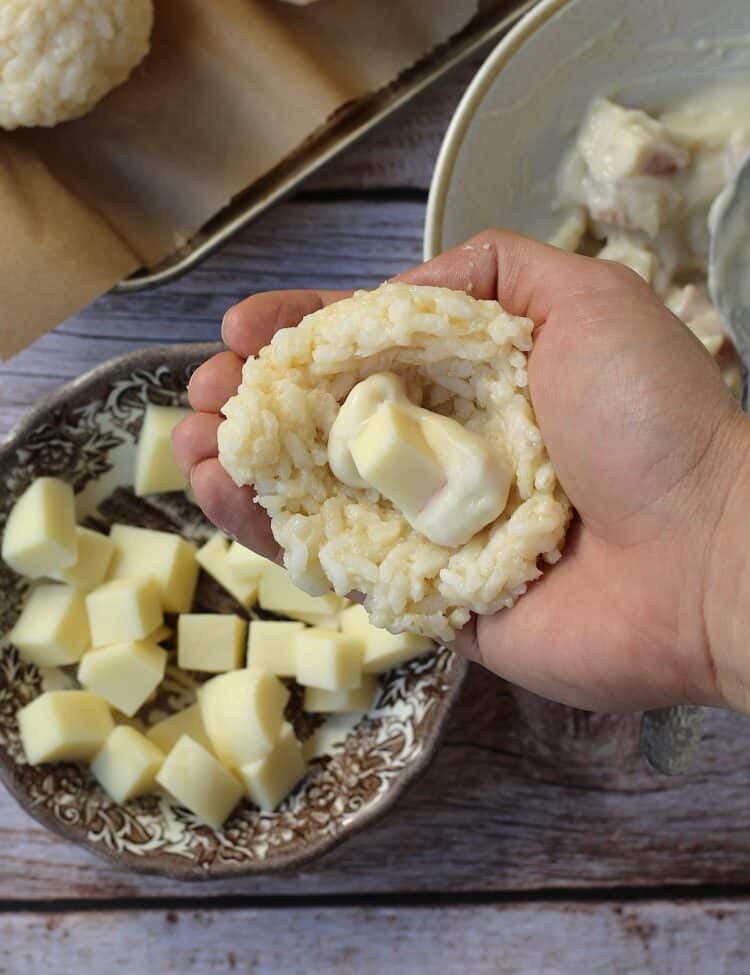 Rice flattened on palm of hand with cheese cube in the center for arancini making.