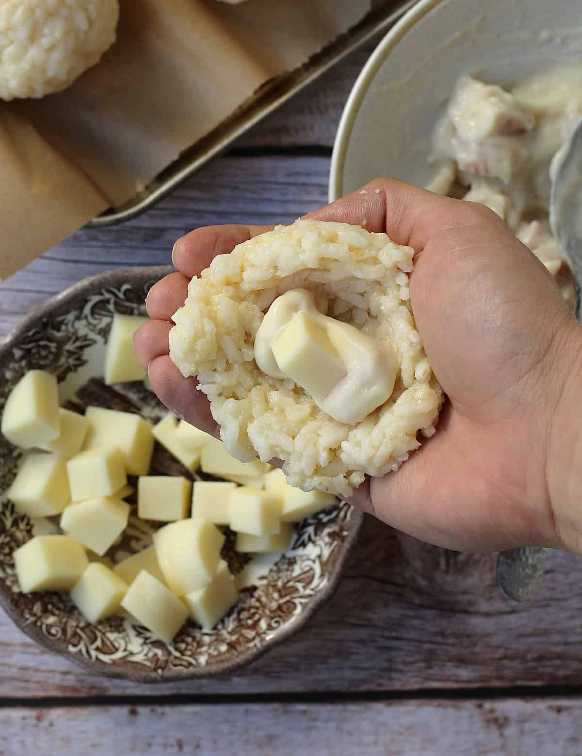 Rice flattened on palm of hand with cheese cube in the center for arancini making.