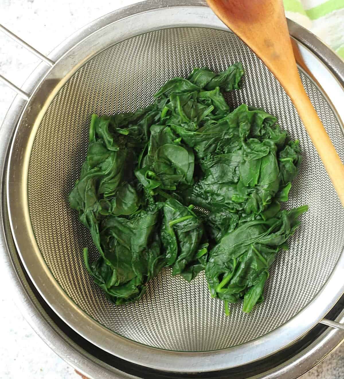 Wilted spinach in colander over bowl to squeeze out excess water.