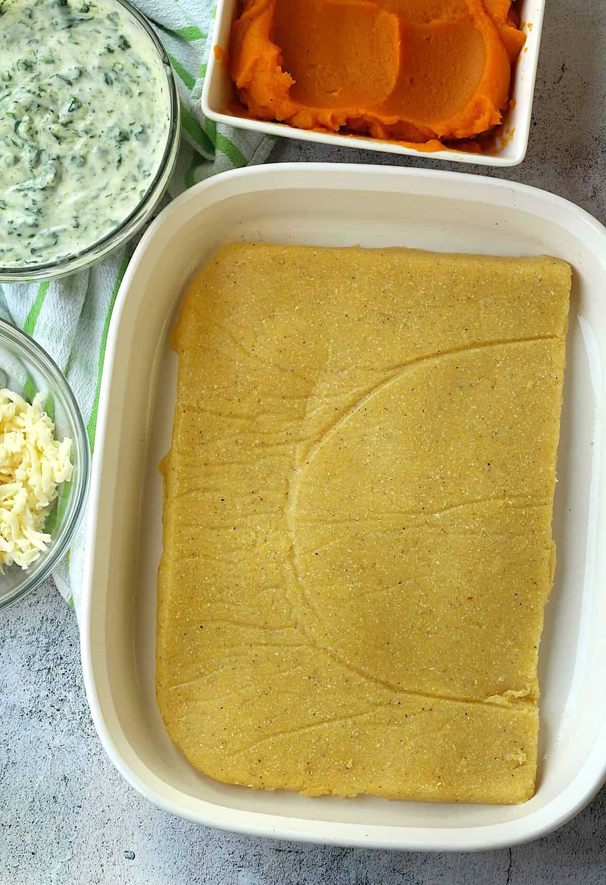 Sheet of polenta placed on the bottom of a casserole dish for polenta lasagna recipe.