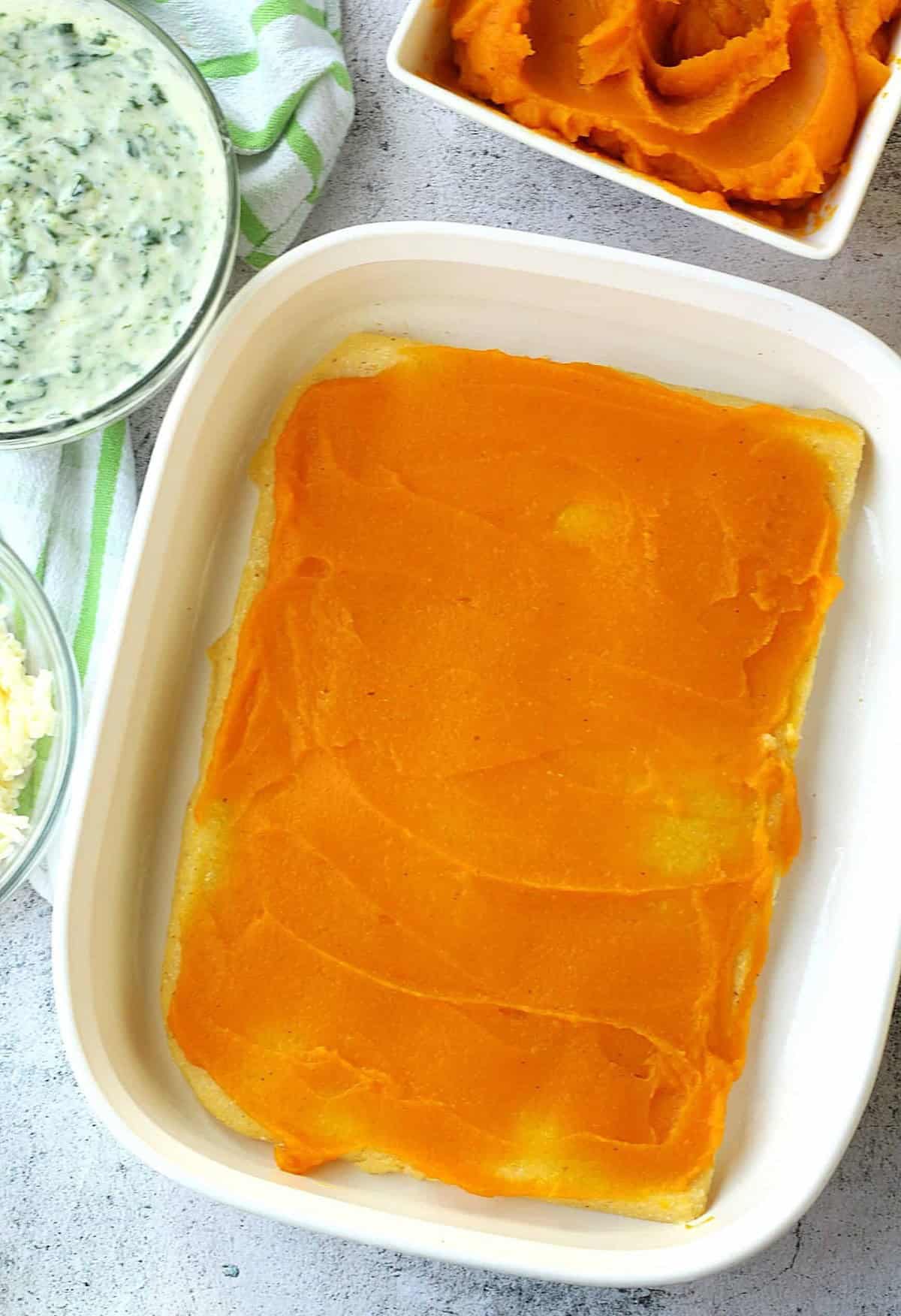 Butternut squash purée spread over polenta in casserole dish.