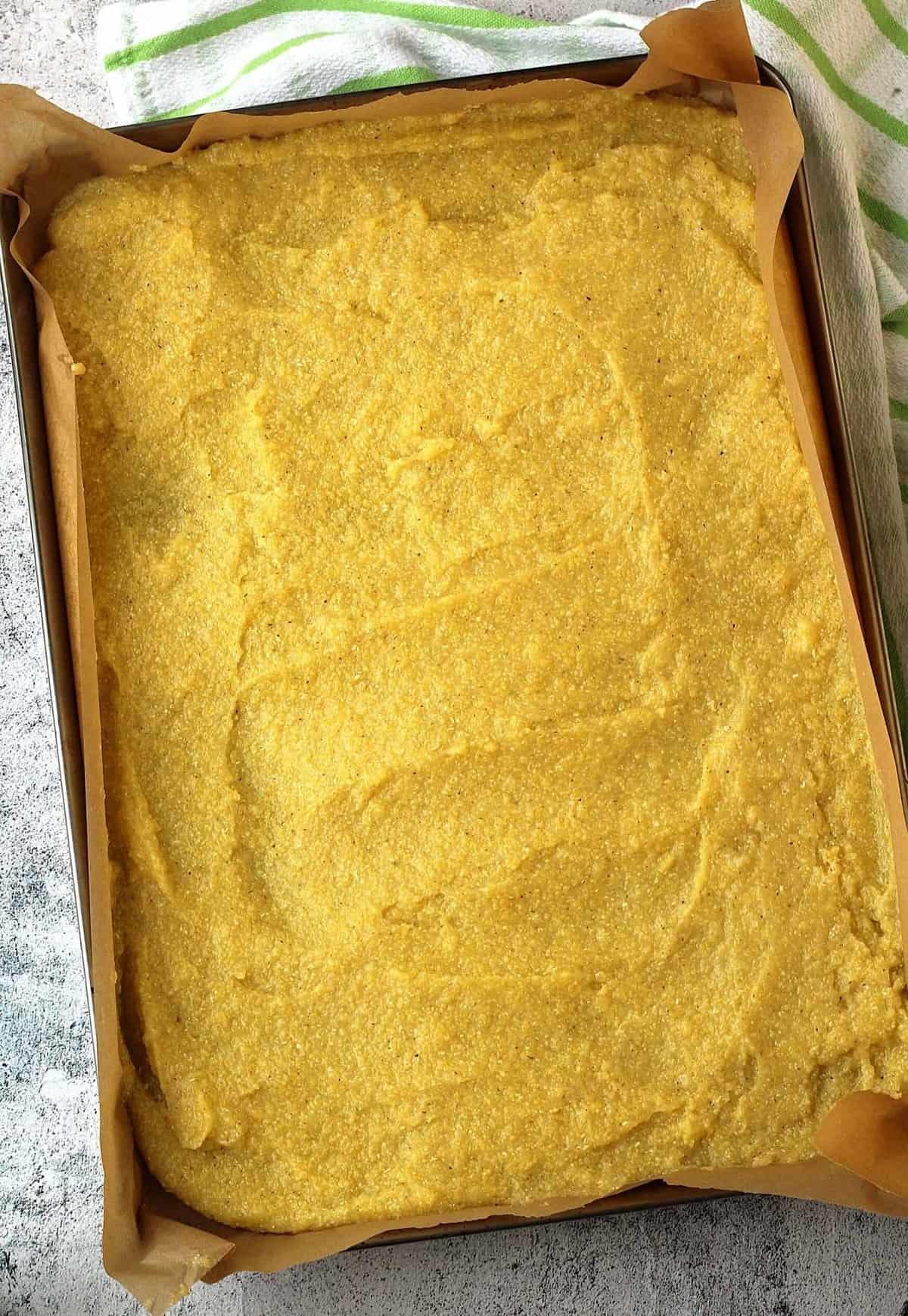 Polenta spread thin on baking sheet lined with parchment paper.