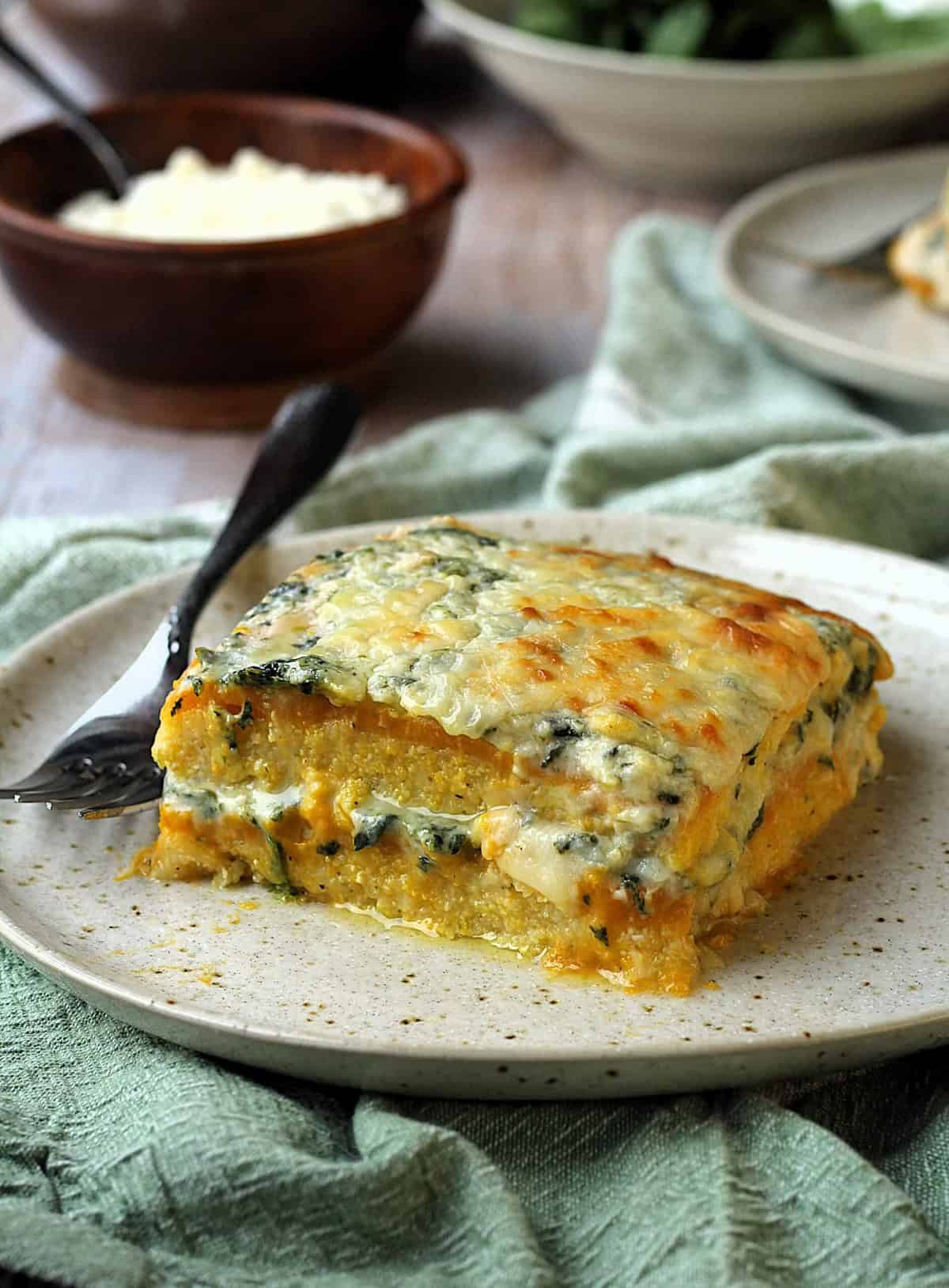 Polenta lasagna layered with butternut squash and spinach béchamel sauce on plate with fork.