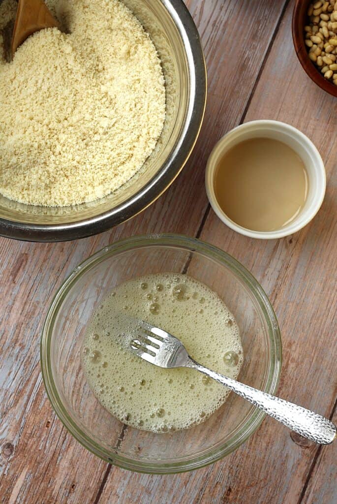 Egg whites whisked in bowl with bowl of almond flour and almond extract next to it.