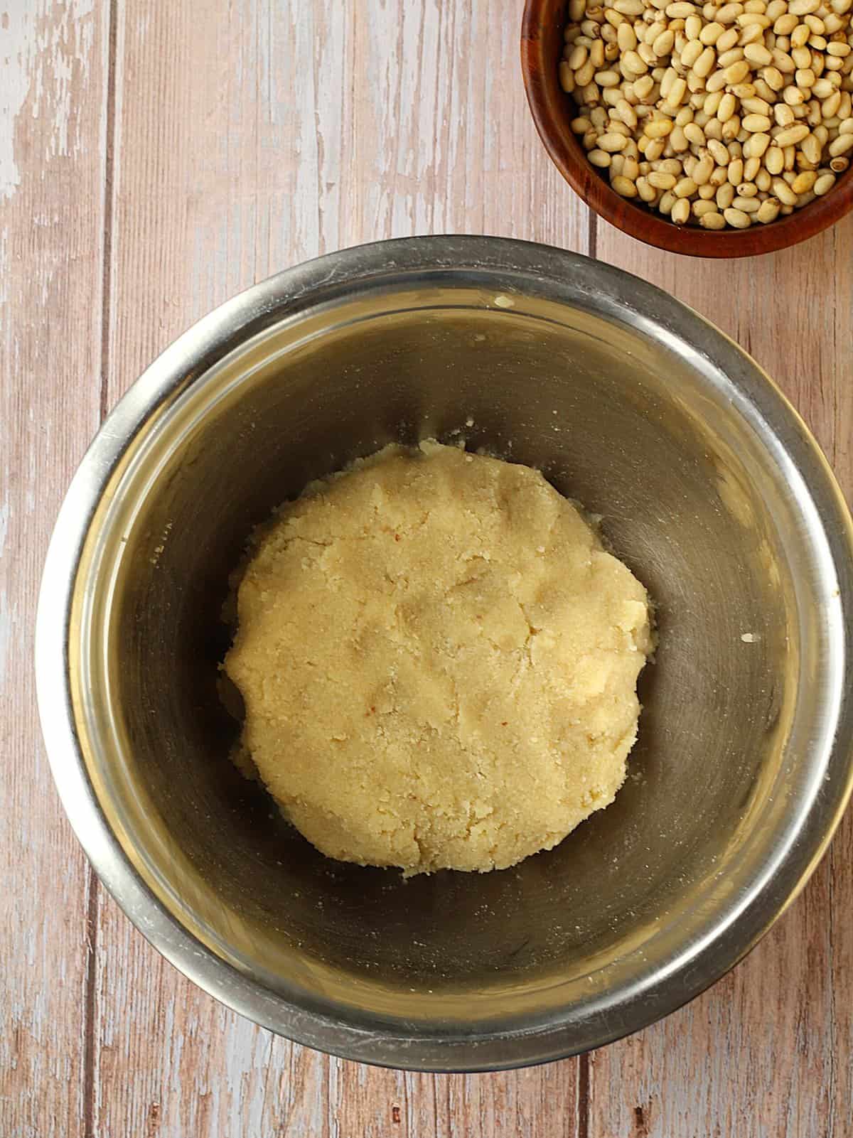 Pignoli cookie dough in bowl with bowl of pine nuts next to it.