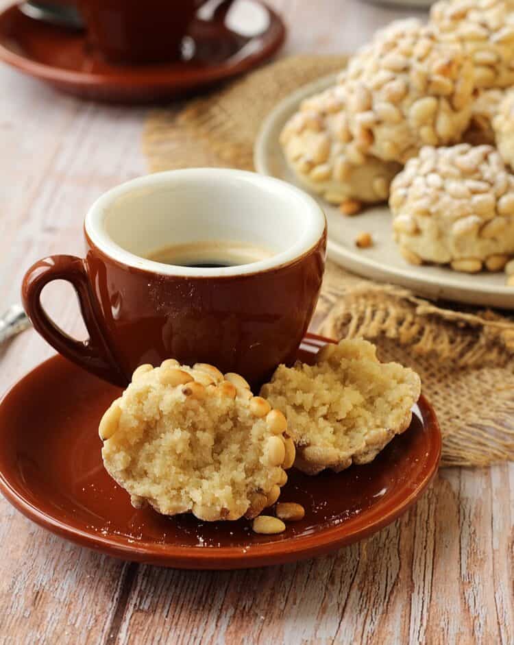 Pignoli cookie cut in half on saucer with cup of coffee.