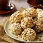 Round plate filled with pignoli cookies with coffee cups next to it.