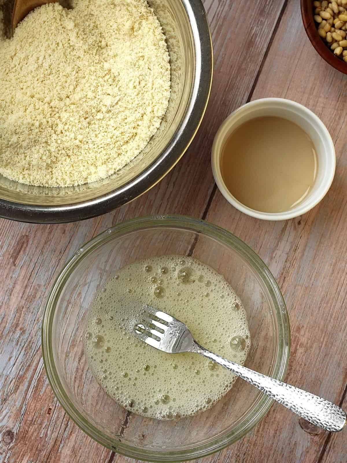 Almond flour in bowl next to bowl with beaten egg whites for pignoli cookie recipe.