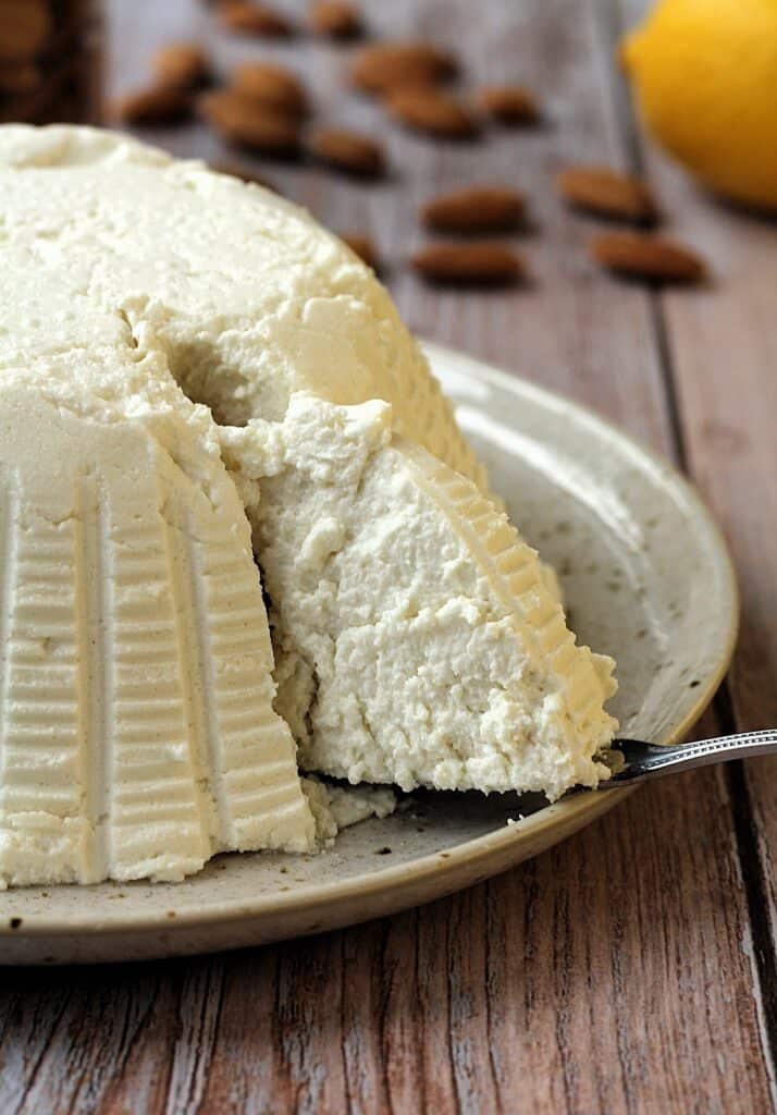 Vegan ricotta with almonds on plate with knife cutting a wedge.