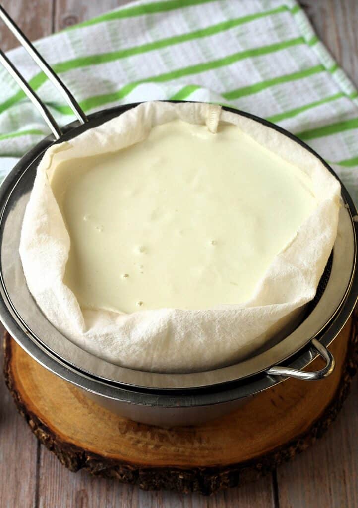 Almond milk ricotta draining in nut milk bag over bowl.