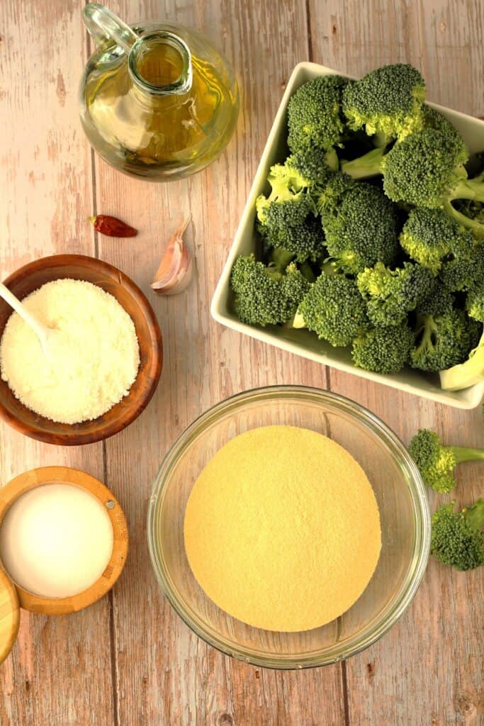 Bowl of broccoli florets, durum wheat flour, salt, grated cheese, olive oil, clove of garlic and red chile.