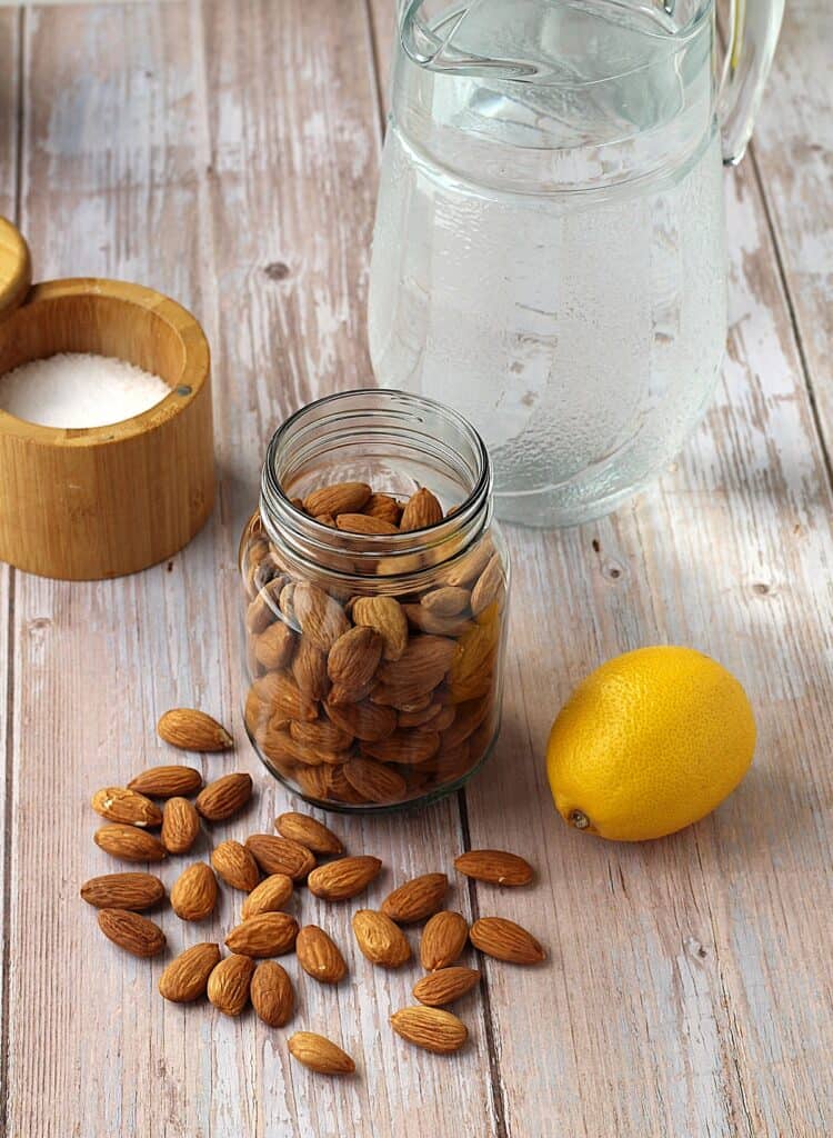 Almonds in jar, lemon, salt and pitcher of water.
