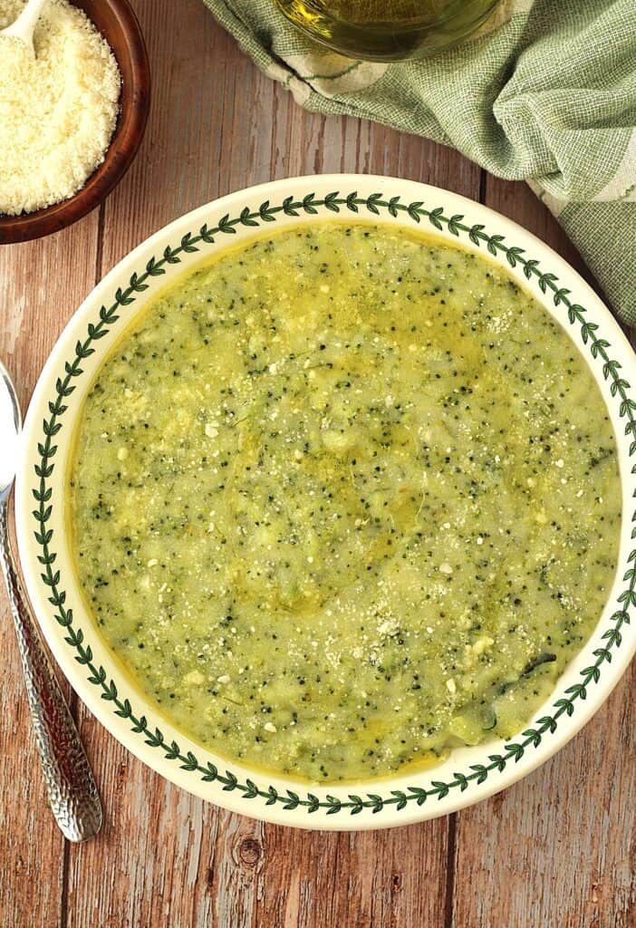 Sicilian polenta with broccoli (frascatula) in bowl with spoon and bowl of cheese on the side.