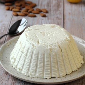 Dairy free ricotta cheese made with almonds on plate with almonds and lemon behind it.